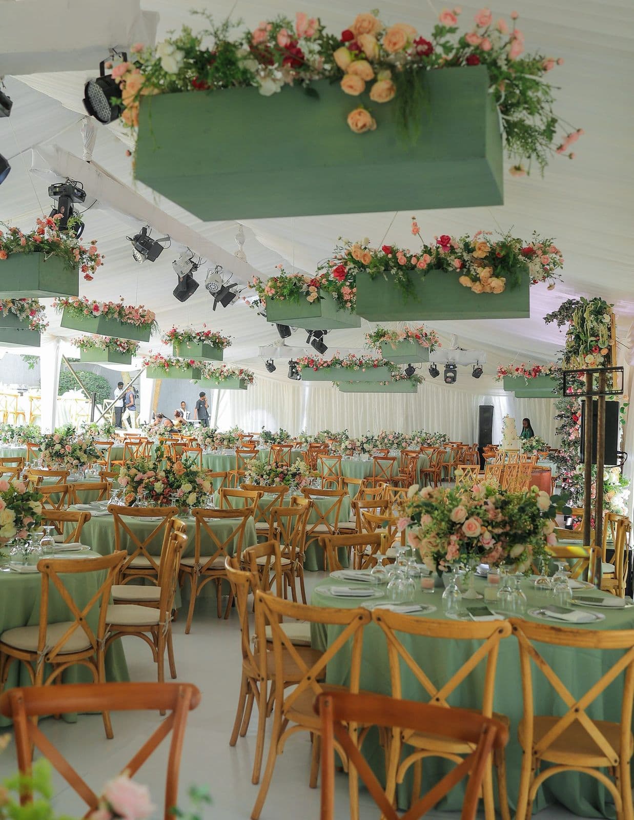 Sage green reception with hanging floral installations and cross-back chairs styled by Modern Charm